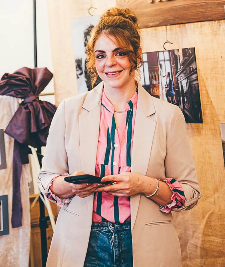Jeanine Büning lächelt mit Blick in die Kamera und einem Mobiltelefon in der Hand